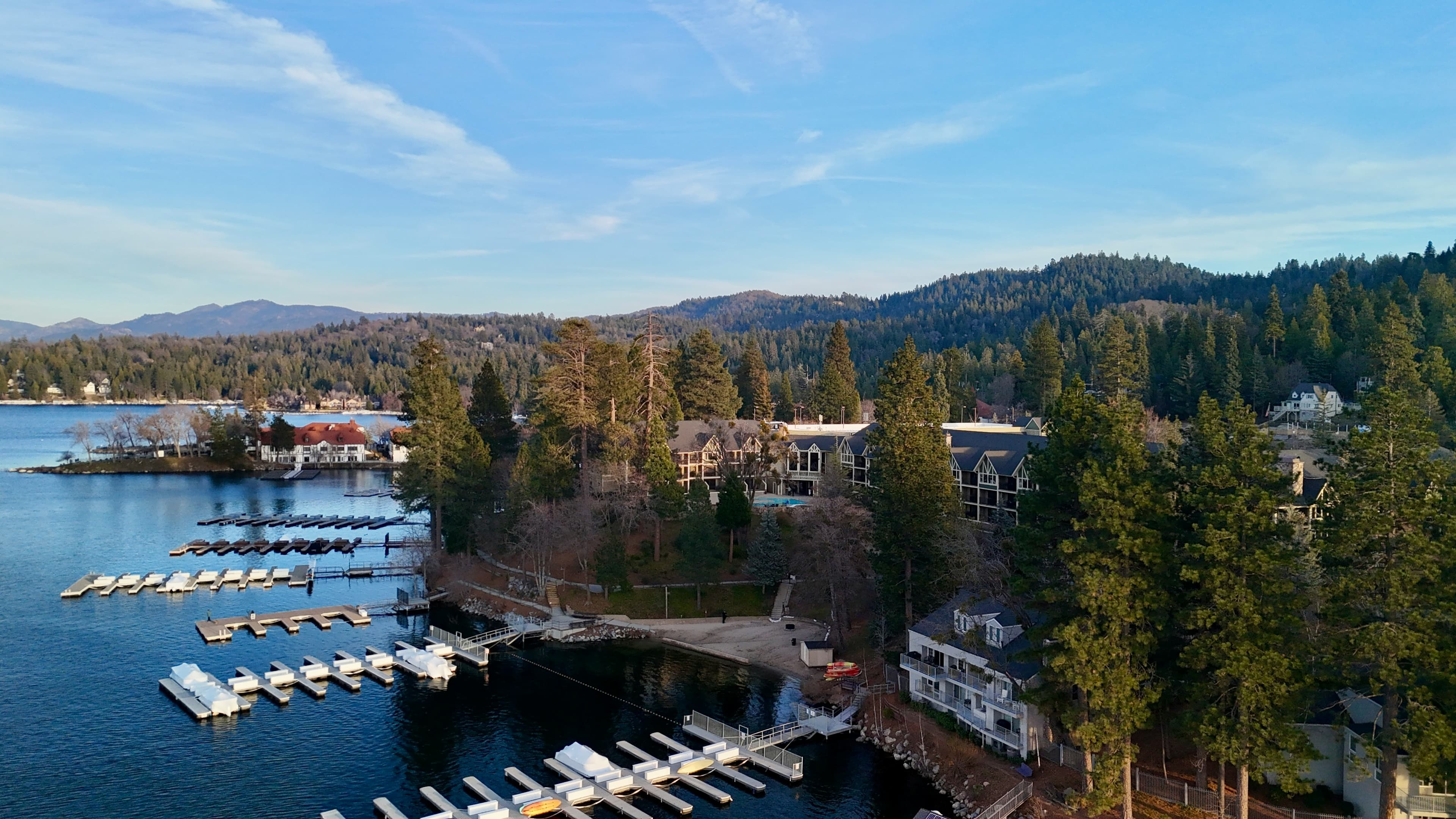 Lake Arrowhead from the air: Lake Arrowhead Resort and Spa among tall pines on the shore, with its pool, beach and boat docks, and the red-roofed buildings of the Village across the water