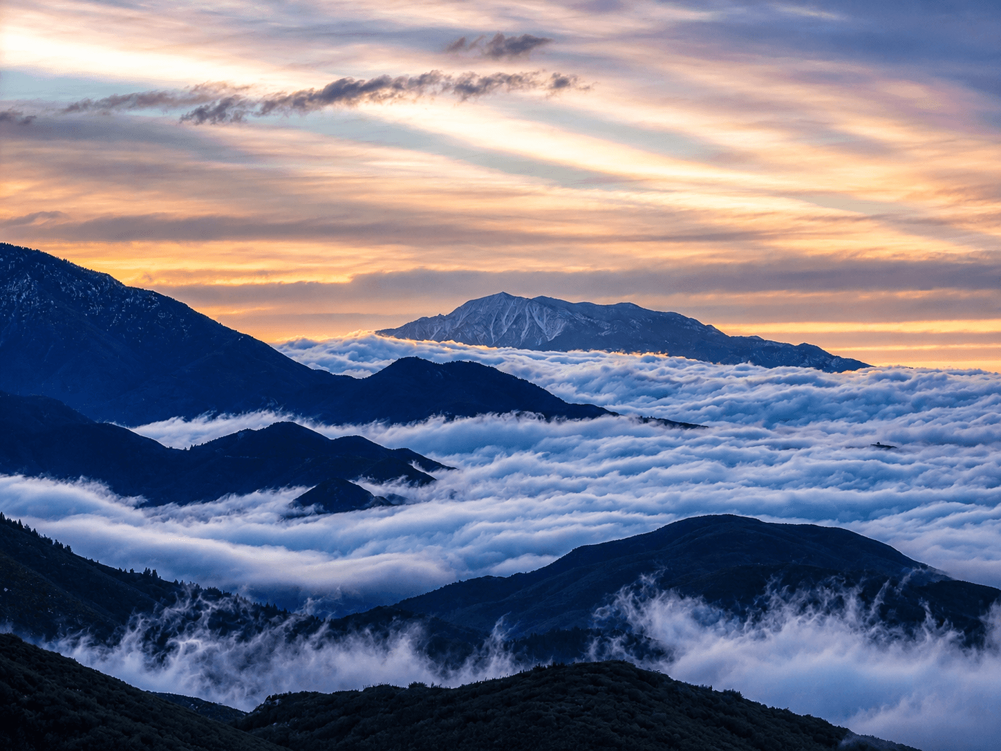 Clouds filling the valleys below the San Bernardino Mountains at sunset, a snow-dusted peak rising above them